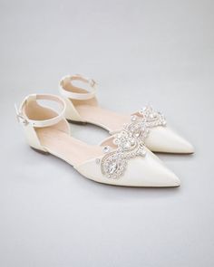 a pair of white shoes with bows and pearls on the toe, sitting on a gray surface