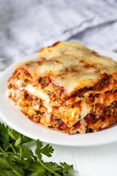 a white plate topped with lasagna covered in sauce and cheese next to parsley