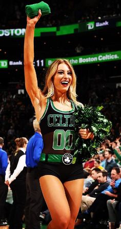 a woman in a cheerleader outfit is holding up a green bottle and some broccoli