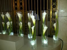 four tall vases filled with white flowers on top of a marble slab in front of a metal gate