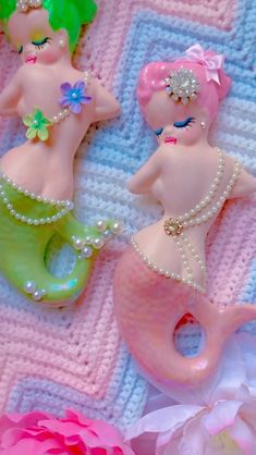 there are two little mermaids that are on the bed together, one is pink and green