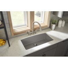 a kitchen sink in front of a window with fruit on the counter and other items