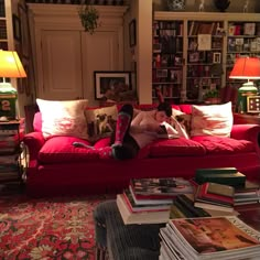 a woman laying on top of a red couch in a living room filled with books