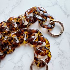 This trendy acrylic chain in Tortoise color features a classic brown dimple print that complements any outfit! With two adjustable O-rings, you can easily shorten the chain to your preferred length. It's the perfect blend of style and versatility, effortlessly matching everything in your wardrobe. Specifications:- 23.5" long without the O-rings- 26.5" long with the O-rings Trendy Brown Chain Jewelry, Trendy Adjustable Tortoiseshell Jewelry, Brown Chain Jewelry As Fashion Accessory, Tortoise Print, Acrylic Bag, Tortoise Color, Classic Brown, Bag Chain, Pull Apart