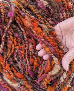 a person holding their hand over a pile of multicolored yarn