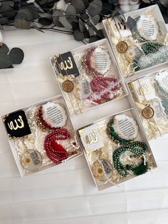 four boxes filled with assorted necklaces on top of a white table next to flowers