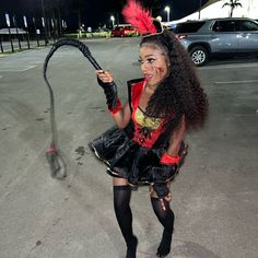 a woman dressed in costume holding a whip with her right hand and posing for the camera