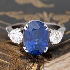 an oval shaped blue sapphire surrounded by three smaller round diamonds sits on top of a book