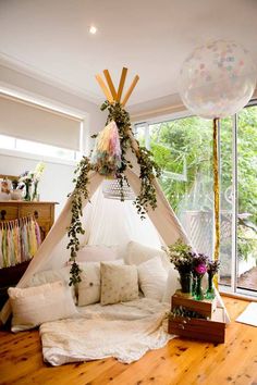 a teepee tent with plants growing out of it and pillows on the floor next to it