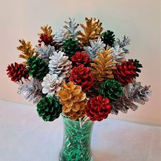 a green vase filled with lots of different colored pine cones and snowflakes