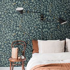 a bed sitting next to a green wall with leaves on it and a wooden chair