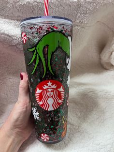 a hand holding a starbucks cup with an alien on it and candy cane in its mouth