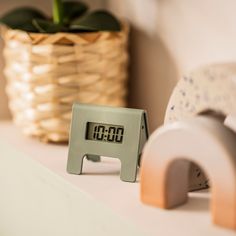 an alarm clock sitting on top of a white shelf next to a potted plant