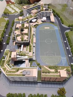 a model of a sports field with buildings and trees in the foreground, and people looking at it