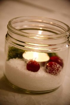 a glass jar filled with white snow and two small red berries sitting on top of it