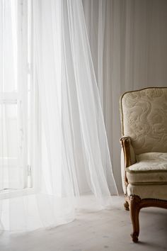 a chair sitting in front of a window covered with white sheer curtains and drapes