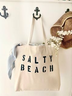 "The SALTY BEACH over sized canvas tote bag is perfect minimalist bag for a trip to the beach! Available with text in several colors... check out the variations! This bag is made from 100% thick, sturdy canvas. AVAILABLE IN TWO SIZES * Large - 19.5\" x 13\" with a 4\" gusset *Jumbo - 23\" x 13\" with a 6\" gusset These bags are hand painted using non-toxic fabric paint. The technique used creates an attractive distressed appearance to the text that varies from bag to bag. All of my products are Trendy Canvas Beach Bag For Beach Season, Trendy Canvas Bag For Beach Season, Natural Cotton Beach Bag For Summer, Natural Cotton Beach Bag For Beach Season, Summer Large Capacity Cotton Beach Bag, Summer Beige Canvas Bag With Letter Print, Large Capacity Cotton Beach Bag For Summer, Beige Cotton Beach Bag For Beach Season, Beige Cotton Bags For Beach Season