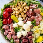 a salad with meat, beans and vegetables in a white bowl on a marble table