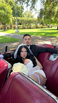 a bride and groom sitting in the back of an old fashioned red car with their arms around each other