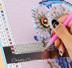 a person is holding a pink pen in front of a cross - stitch pattern on a computer screen