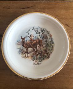 a plate with two deer on it sitting on top of a wooden table next to a wall