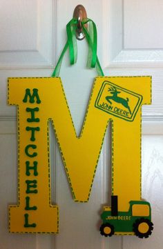 a door hanger with the letter m and a toy tractor hanging from it's side