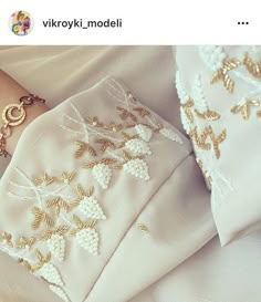 a woman's hand is shown next to some white fabric with gold embroidered designs on it