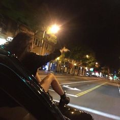 a man driving down the street at night with his hand up in the air,