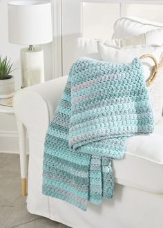 a crocheted blanket sitting on top of a white couch next to a lamp