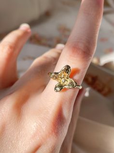 a person's hand with a gold ring on top of their finger and an orange object in the background