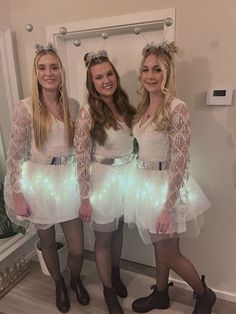 three women dressed up in white dresses and headbands posing for the camera with their arms around each other