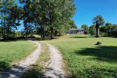 a dirt road leading to a house in the middle of a green field with trees