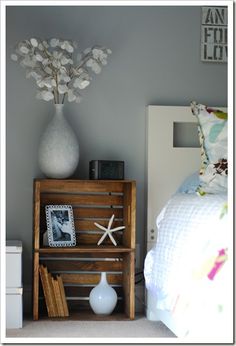 a white vase sitting on top of a wooden crate next to a bed with pillows