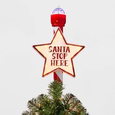 a lighted sign that says santa stop here on top of a christmas tree in front of a white sky