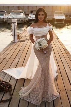 a woman standing on a dock wearing a dress with lace overlay and off the shoulder sleeves