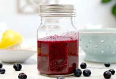 a glass jar filled with blueberries next to a bowl of lemons and water