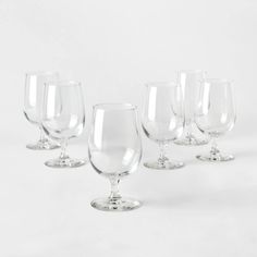 six empty wine glasses lined up against a white background