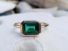 an emerald colored ring sitting on top of a white pillow