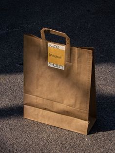 a brown paper bag sitting on the ground with a yellow tag hanging from it's handle