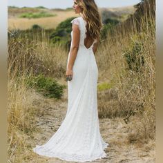 a woman in a white dress standing on a dirt road with tall grass behind her