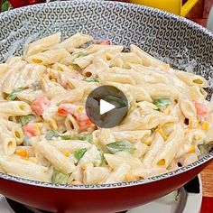 a red bowl filled with pasta and vegetables on top of a table next to utensils