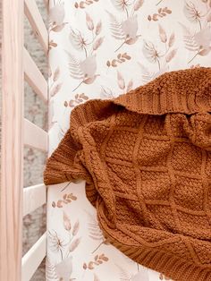 a brown knitted blanket laying on top of a white crib