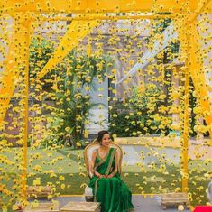 a woman sitting on a bench in front of a yellow and white backdrop with flowers