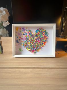 a heart made out of colorful confetti in a white frame on a table