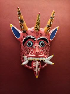 a mask hanging on the side of a red wall with horns and fangs attached to it