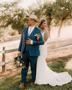 a bride and groom standing in front of a fence holding each other with their arms