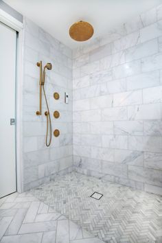 a walk in shower sitting next to a white tiled wall and floor with gold fixtures