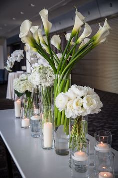 white flowers and candles are lined up on a table