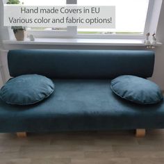 a blue couch sitting in front of a window with two pillows on top of it