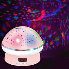 an alarm clock sitting on top of a colorful light projector in front of a black background